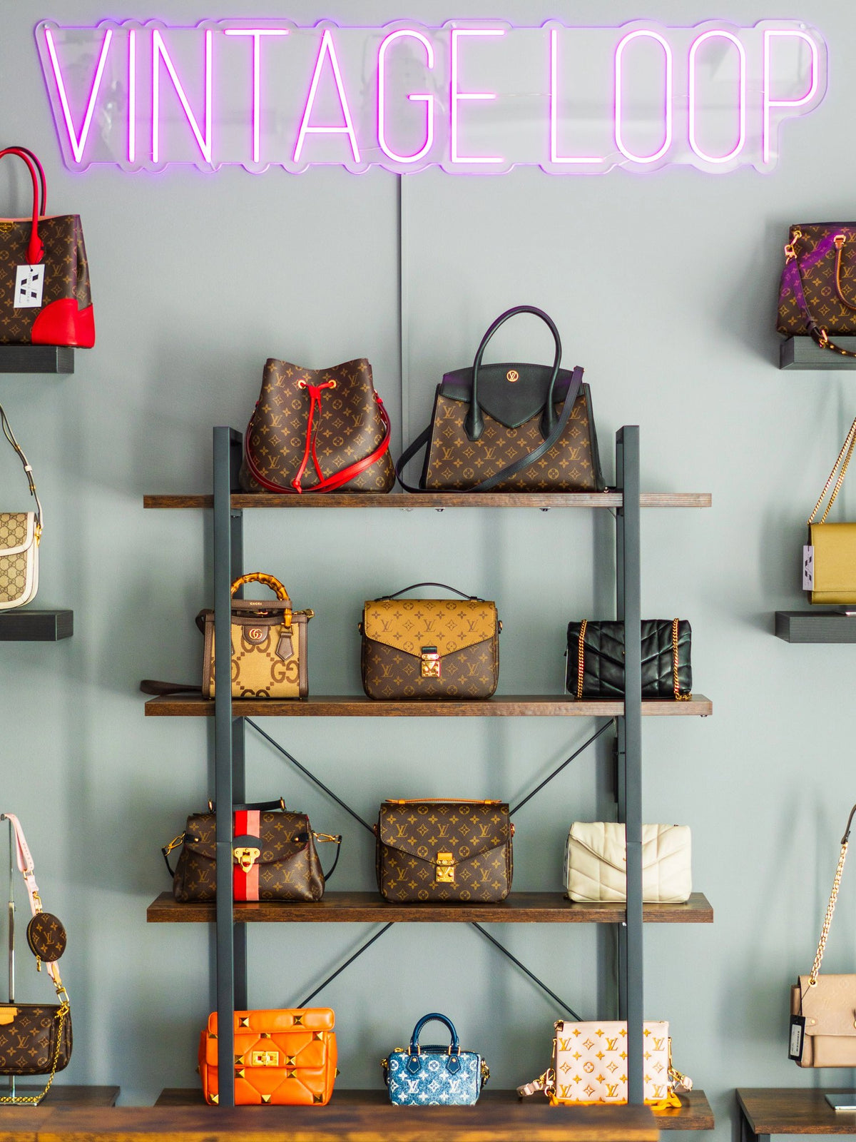 Interno del negozio Vintage Loop: borse di lusso second-hand esposte sugli scaffali sotto l'insegna al neon